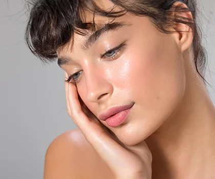 Peaceful brunette woman, resting her face in her hand against a grey background - Chin Implant in San Francisco, CA