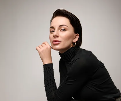 Woman with short brown hair, in black turtle neck, and hand rested next to face - Facial Fillers in San Francisco, CA