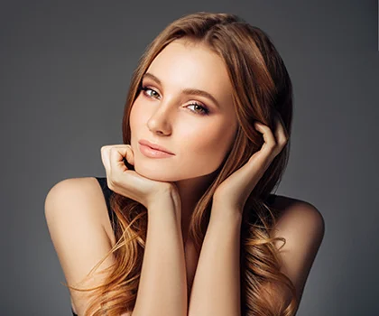 Blonde woman, resting chin in hand, against a grey backdrop - Facial Implants in San Francisco, CA