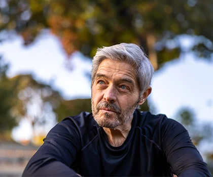 Senior man in a black long sleeve, sitting peacefully in a park, in front of a tree - Skin Cancer Reconstruction in San Francisco, CA